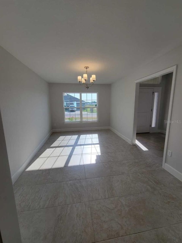 tiled spare room with a chandelier