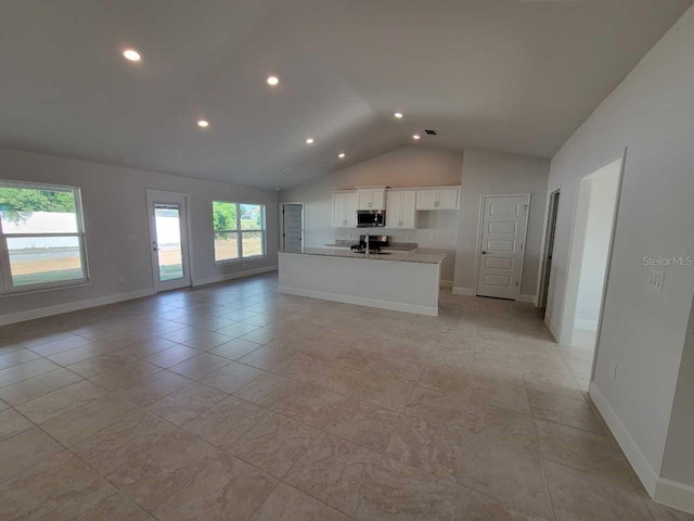 unfurnished living room with sink, light tile patterned floors, a healthy amount of sunlight, and lofted ceiling