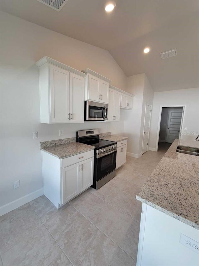 kitchen featuring lofted ceiling, stainless steel appliances, sink, light stone countertops, and white cabinets