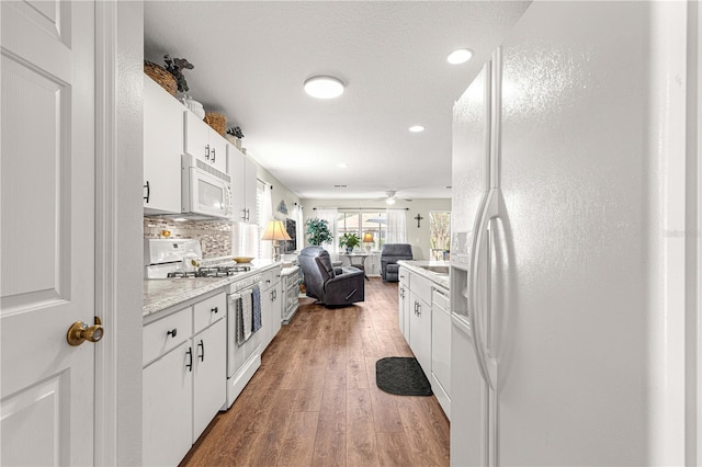 kitchen with decorative backsplash, white appliances, hardwood / wood-style flooring, and white cabinetry