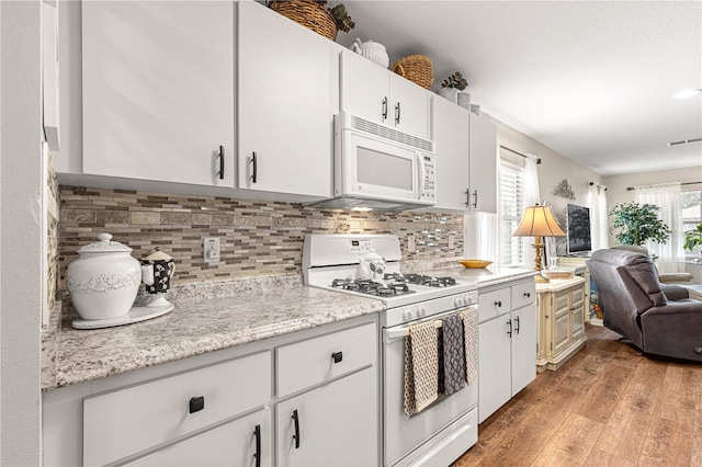 kitchen featuring white appliances, white cabinets, hardwood / wood-style flooring, tasteful backsplash, and light stone counters