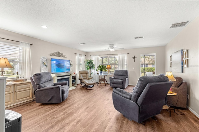 living room featuring ceiling fan, a textured ceiling, and light hardwood / wood-style flooring