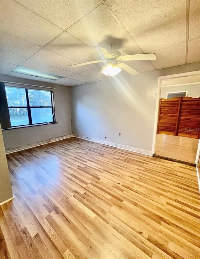 spare room with a drop ceiling, hardwood / wood-style floors, and ceiling fan