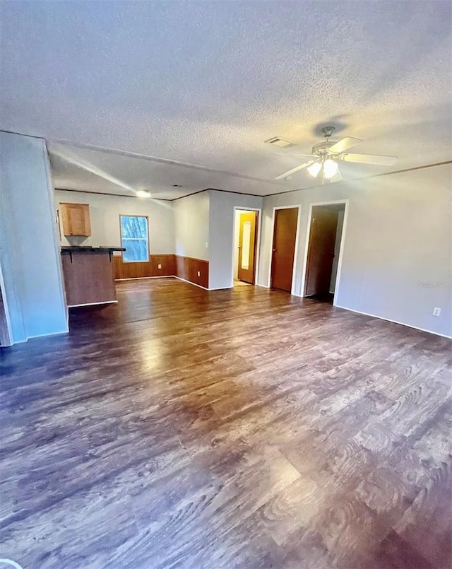 unfurnished living room featuring dark wood-type flooring, a textured ceiling, and ceiling fan