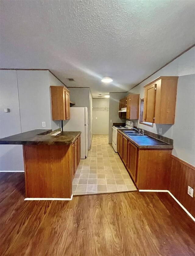 kitchen with white appliances, sink, light wood-type flooring, a textured ceiling, and kitchen peninsula