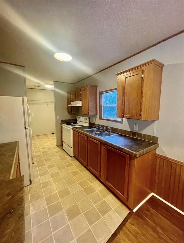 kitchen featuring light tile patterned floors, a textured ceiling, sink, wooden walls, and white appliances