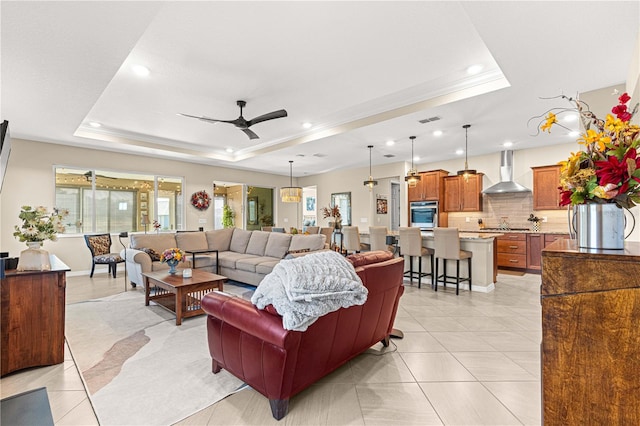 living room with ornamental molding, ceiling fan, light tile patterned flooring, and a raised ceiling