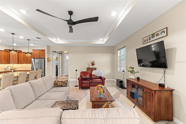 living room featuring crown molding, a barn door, a tray ceiling, and ceiling fan