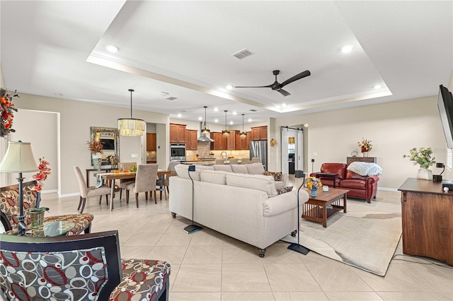 living room with ceiling fan, a raised ceiling, light tile patterned flooring, and a barn door