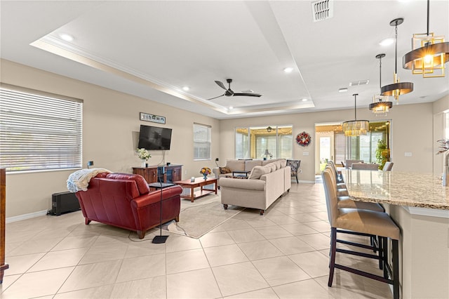 living room with ceiling fan, light tile patterned flooring, ornamental molding, and a tray ceiling