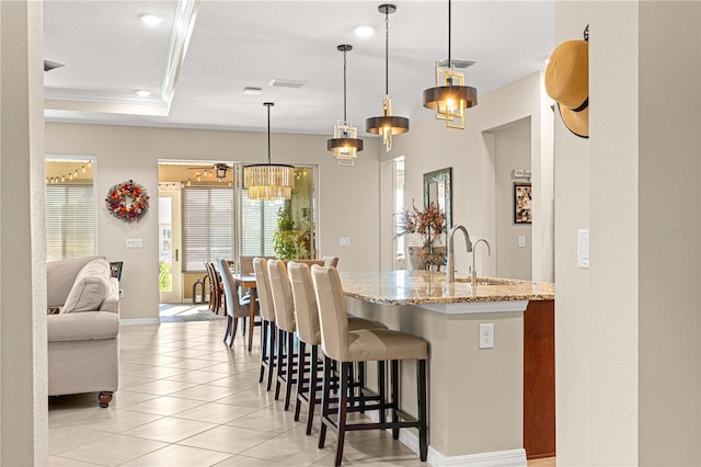 kitchen featuring light tile patterned floors, sink, decorative light fixtures, light stone counters, and a breakfast bar area