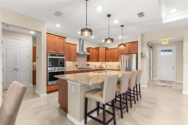 kitchen featuring a kitchen island with sink, wall chimney range hood, sink, pendant lighting, and appliances with stainless steel finishes