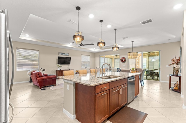 kitchen with appliances with stainless steel finishes, sink, an island with sink, pendant lighting, and light stone counters