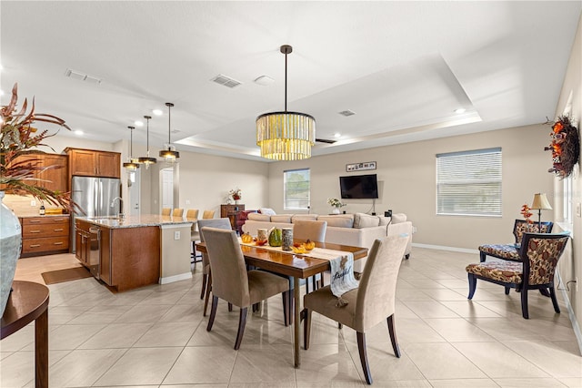 tiled dining area with a raised ceiling, sink, and a chandelier