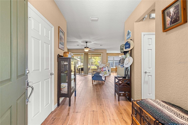 hallway with a textured ceiling and light wood-type flooring