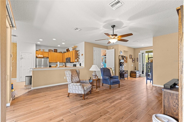 living room with ceiling fan, a textured ceiling, and light wood-type flooring