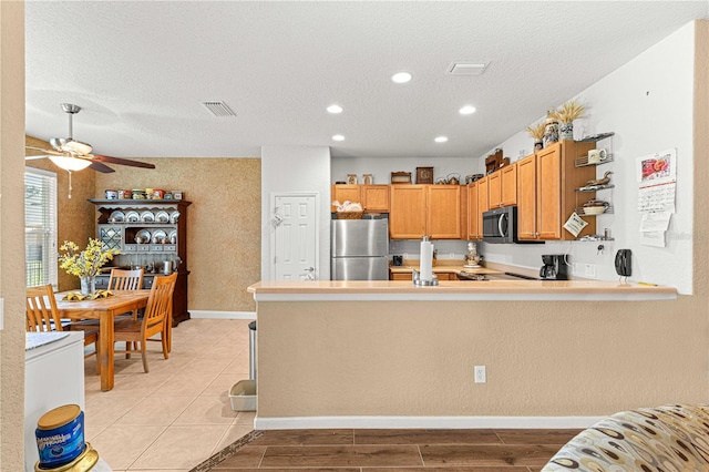 kitchen with light wood-type flooring, stainless steel appliances, a textured ceiling, and kitchen peninsula