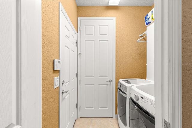 clothes washing area with washer and clothes dryer, a textured ceiling, and light tile patterned flooring