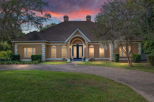 single story home with a yard, a chimney, stucco siding, and curved driveway