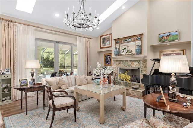 living room with high vaulted ceiling, wood-type flooring, a skylight, a fireplace, and a notable chandelier