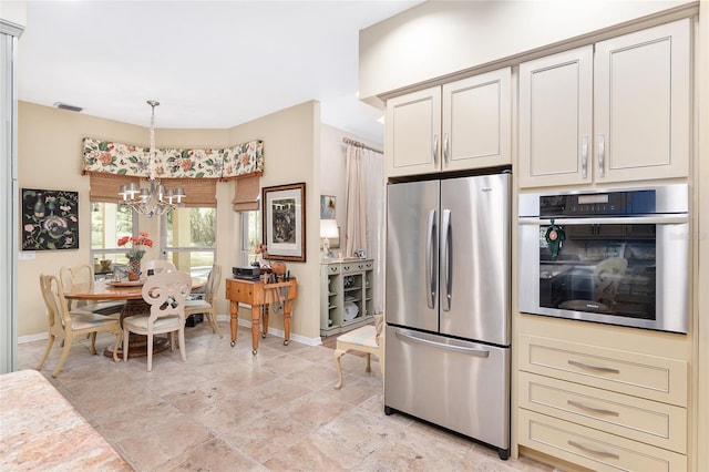 kitchen featuring appliances with stainless steel finishes, cream cabinetry, a notable chandelier, and pendant lighting