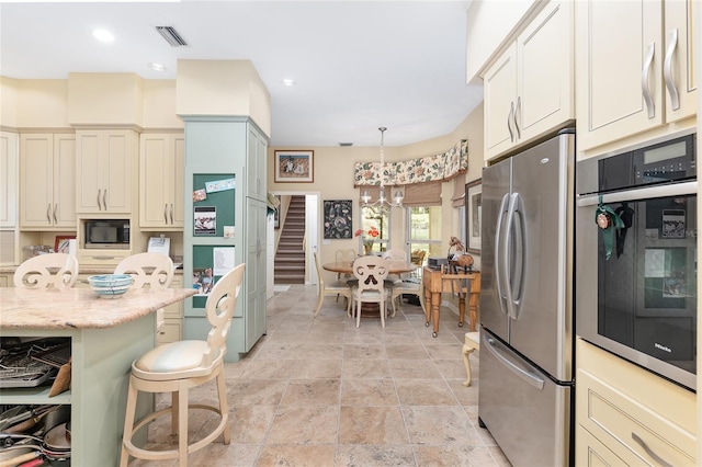 kitchen featuring cream cabinetry, hanging light fixtures, stainless steel appliances, a breakfast bar, and light stone counters