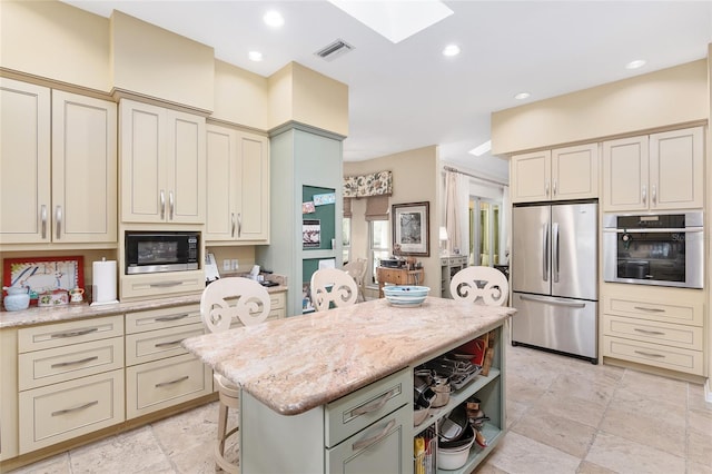 kitchen with cream cabinets, a skylight, a center island, stainless steel appliances, and light stone counters