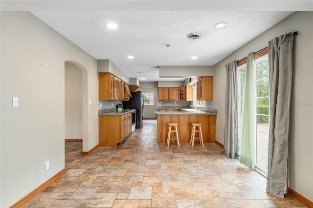 kitchen featuring a breakfast bar area, kitchen peninsula, a textured ceiling, and a wealth of natural light