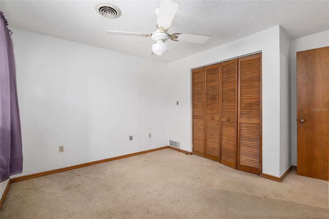 unfurnished bedroom featuring a textured ceiling, light colored carpet, a closet, and ceiling fan