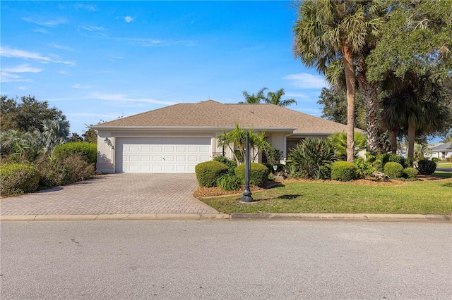 single story home with stucco siding, a garage, a front lawn, and decorative driveway