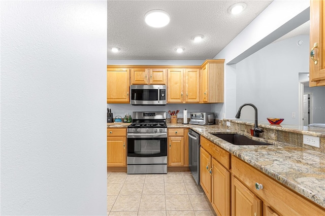 kitchen with sink, stainless steel appliances, light stone counters, kitchen peninsula, and light tile patterned floors