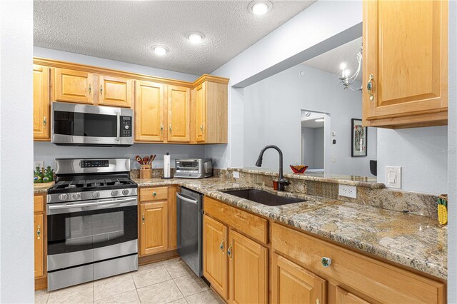 kitchen with a sink, stainless steel appliances, a textured ceiling, light tile patterned floors, and light stone countertops