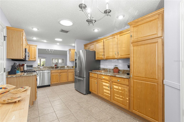 kitchen featuring light stone countertops, appliances with stainless steel finishes, an inviting chandelier, and sink