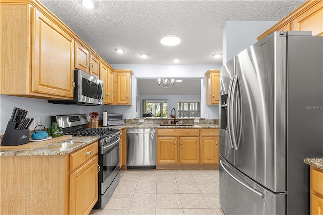 kitchen with a sink, an inviting chandelier, light stone counters, and appliances with stainless steel finishes