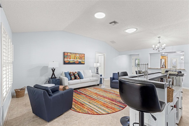 living area featuring a textured ceiling, visible vents, vaulted ceiling, a chandelier, and baseboards