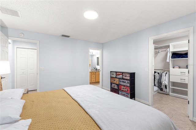 bedroom featuring ensuite bathroom, a walk in closet, a textured ceiling, light tile patterned flooring, and a closet