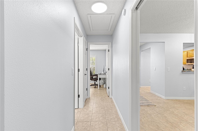 hallway featuring light tile patterned floors, baseboards, and a textured ceiling