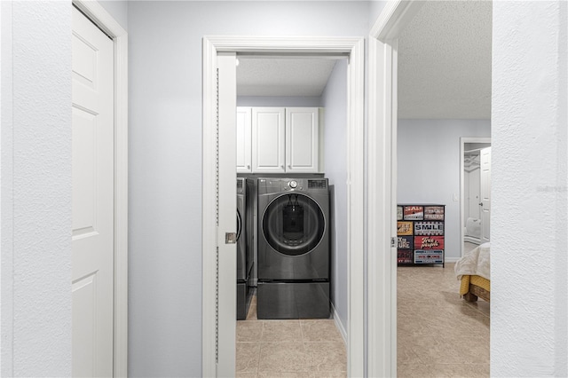 laundry area featuring cabinets, light tile patterned floors, a textured ceiling, and washing machine and clothes dryer