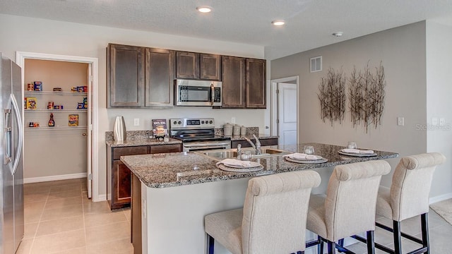 kitchen featuring dark stone countertops, a kitchen island with sink, stainless steel appliances, and a breakfast bar area