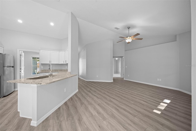 kitchen with sink, light stone counters, stainless steel fridge, white cabinets, and light wood-type flooring