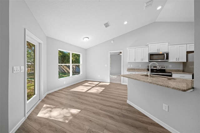 kitchen featuring light hardwood / wood-style flooring, vaulted ceiling, light stone countertops, appliances with stainless steel finishes, and white cabinetry