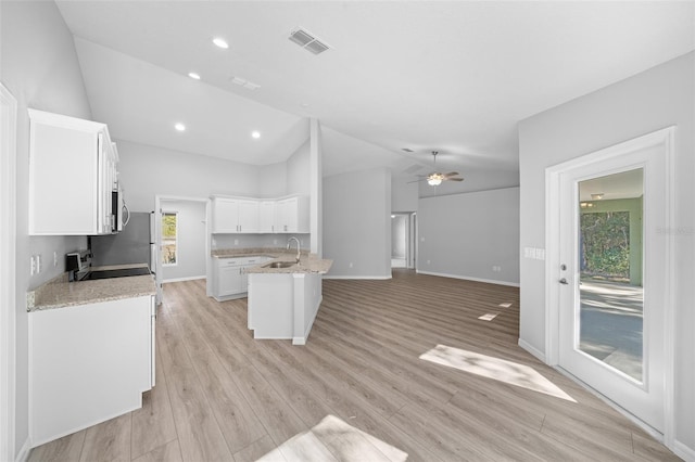 kitchen featuring sink, vaulted ceiling, light wood-type flooring, light stone counters, and white cabinetry