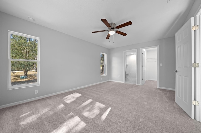 unfurnished bedroom with ceiling fan, a spacious closet, light carpet, and connected bathroom