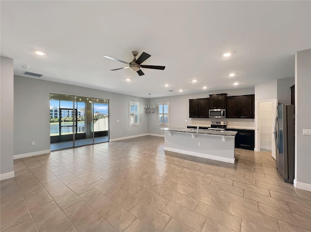 kitchen with a kitchen breakfast bar, a center island with sink, light tile patterned floors, appliances with stainless steel finishes, and ceiling fan with notable chandelier