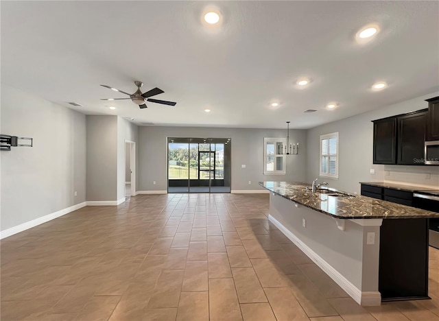 kitchen featuring appliances with stainless steel finishes, sink, ceiling fan with notable chandelier, a kitchen breakfast bar, and a center island with sink