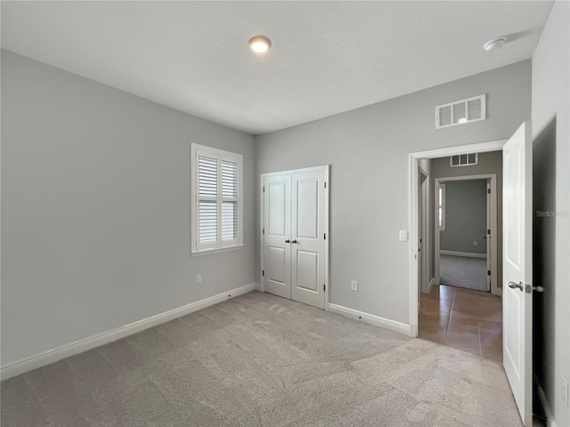 unfurnished bedroom featuring a closet, a textured ceiling, and light colored carpet