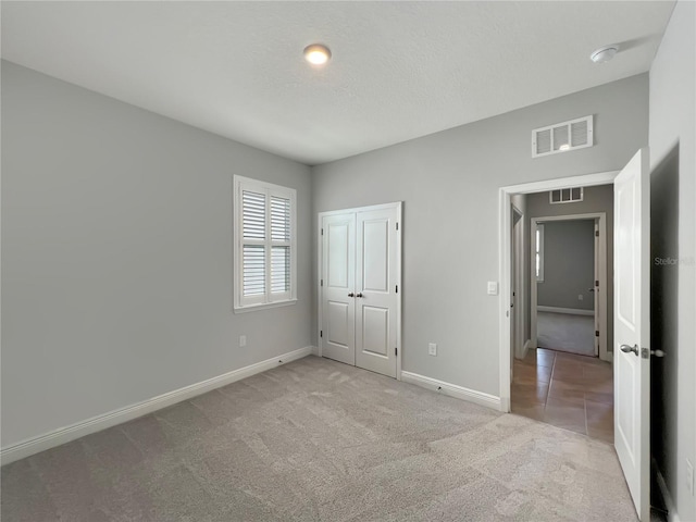 unfurnished bedroom featuring a closet, visible vents, baseboards, and light carpet