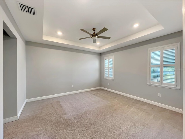 carpeted spare room featuring a raised ceiling, baseboards, and visible vents