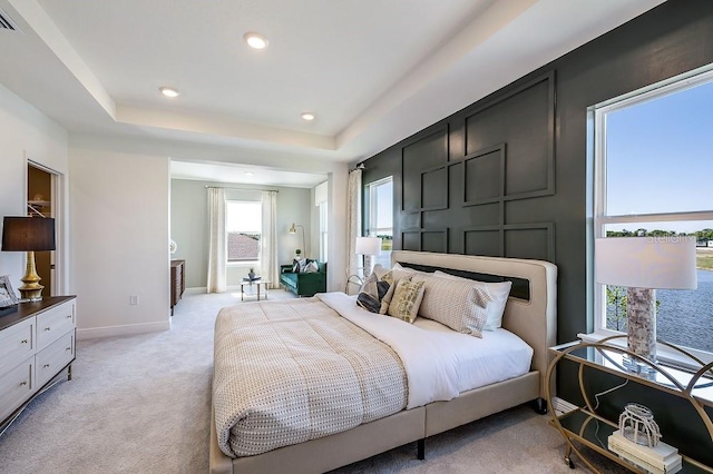 bedroom with light colored carpet and a tray ceiling