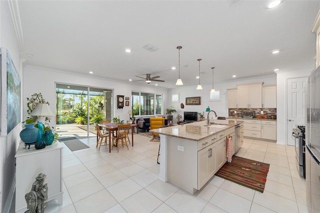 kitchen with an island with sink, hanging light fixtures, light stone countertops, light tile patterned floors, and ceiling fan